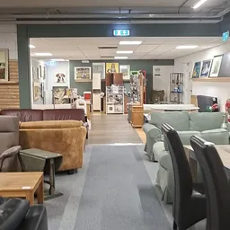 Winkelvloer met bruine en groene fauteuils, houten tafels, stellingen met decoraties en foto's aan de muren