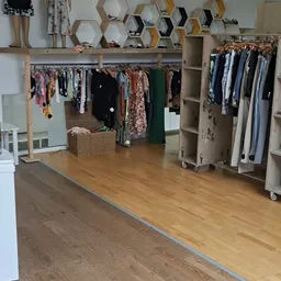 Winkelinterieur met kledingrekken vol tweedehands kleding, houten vloer en stellingen