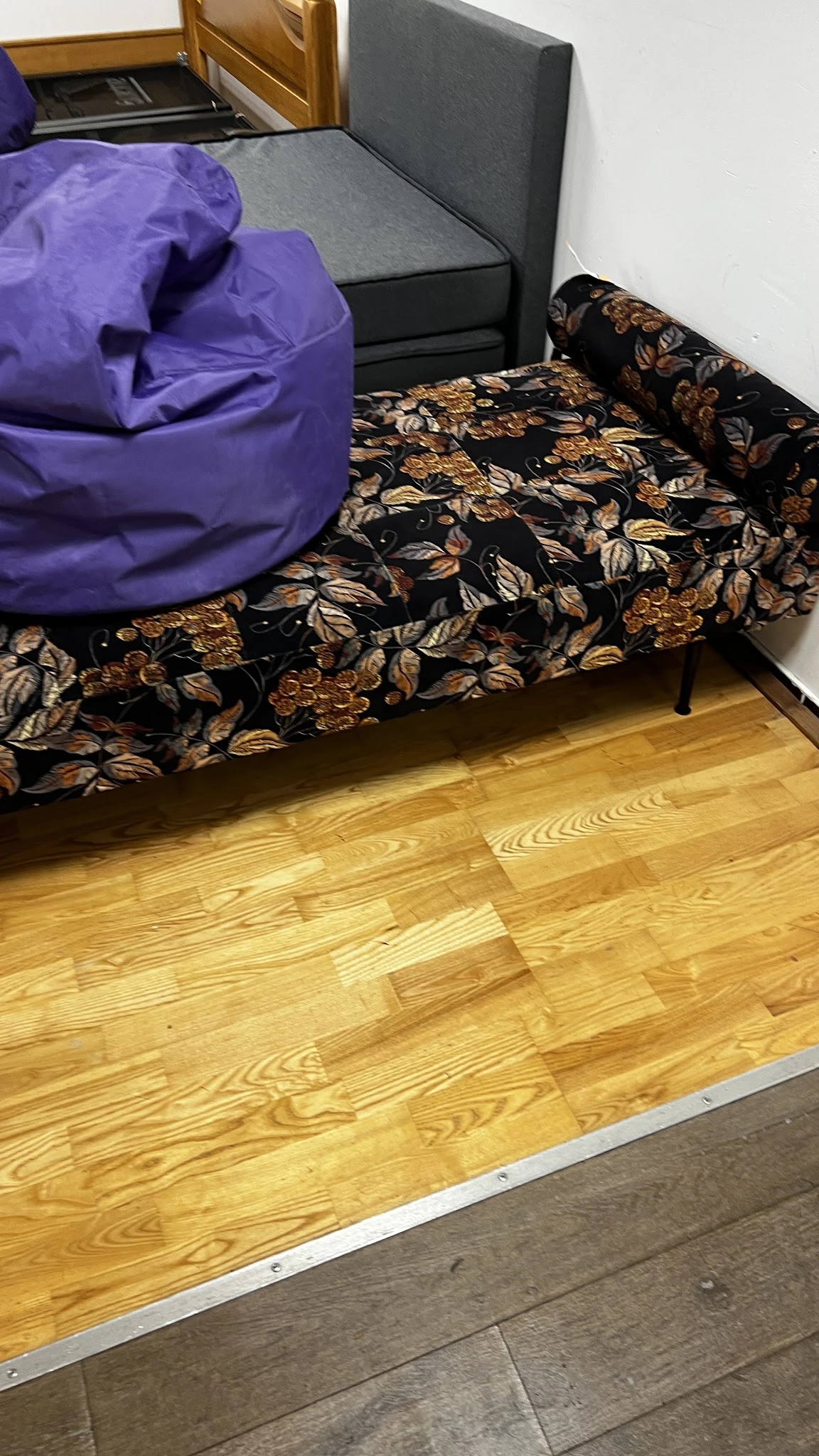 Houten vloer met gedeelte van een gemoebleerd bed met paars en zwart gemotiveerd textiel