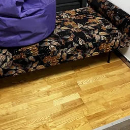 Houten vloer met gedeelte van een gemoebleerd bed met paars en zwart gemotiveerd textiel
