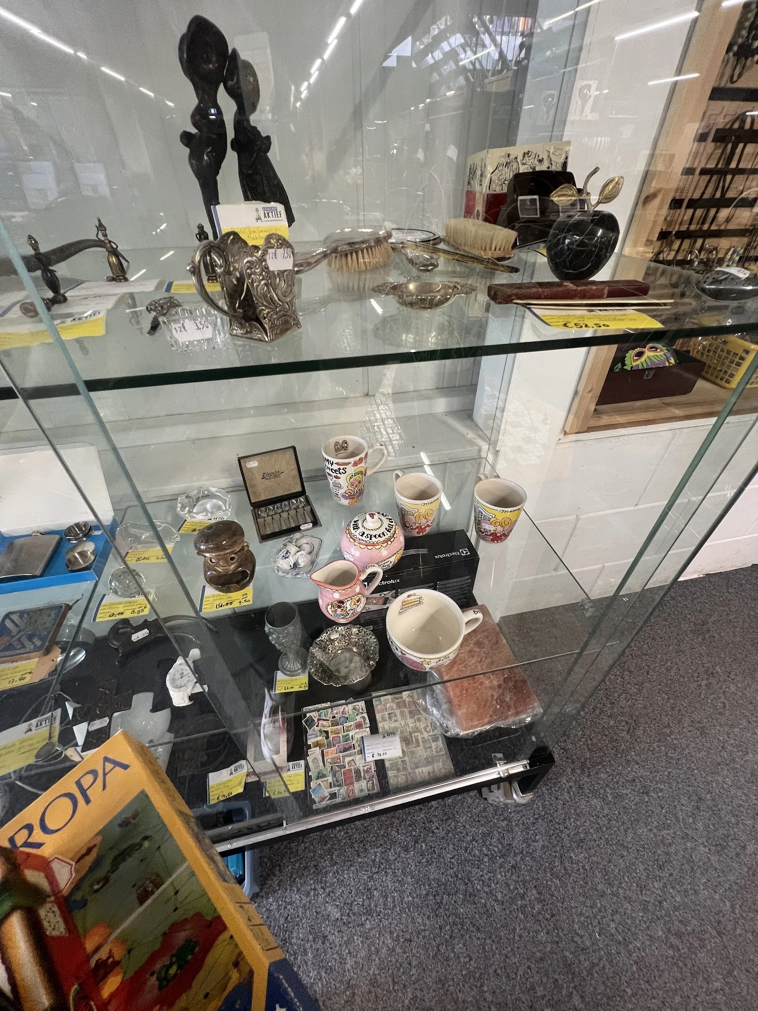 Glazen vitrinekast met diverse huishoudelijke artikelen zoals servies, bekers, decoratieve items en vintage spullen