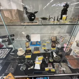 Glazen vitrinekast met diverse tweedehands artikelen zoals servies, accessoires en decoratieve items met gele prijskaartjes