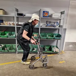 Medewerker in witte helm en zwart vest demonstreert een tweewielig voertuig in de winkel met groene stellingkasten op de acht