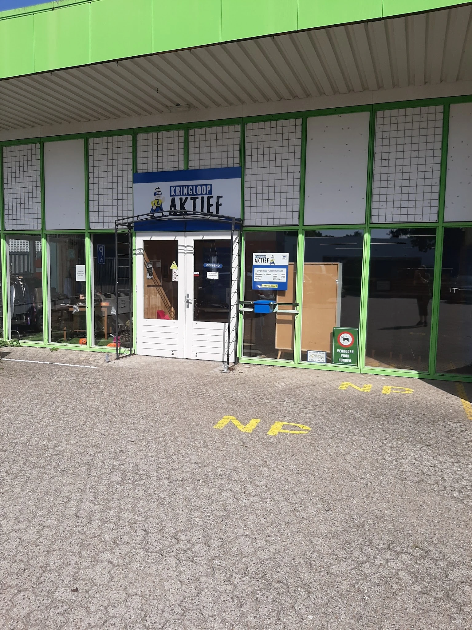 Voorgevel van Kringloop Aktief met groene raamkozijnen, witte deur en winkelnaam op bord boven ingang