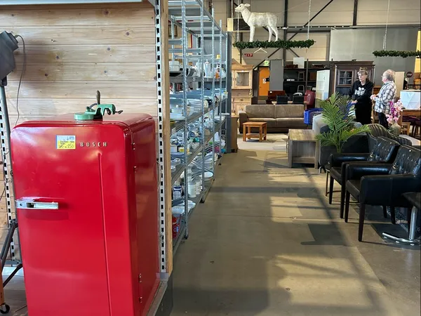 Winkelvloer van kringloopwinkel met rode Bosch-koelkast, stellingen, planten en bezoekers in het pand