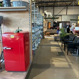 Winkelvloer van kringloopwinkel met rode Bosch-koelkast, stellingen, planten en bezoekers in het pand