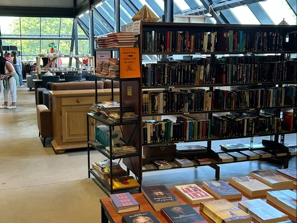 Winkelinterieur met boekenrekken, houten meubels en glazen dak; klanten in de achtergrond