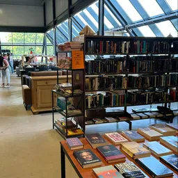 Winkelinterieur met boekenrekken, houten meubels en glazen dak; klanten in de achtergrond