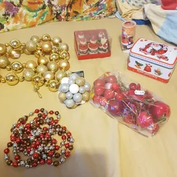 Uitgestalde kerstversiering en decoraties op een tafel: gouden en rode ballen, slingers, kaarsen en kerstdoosjes
