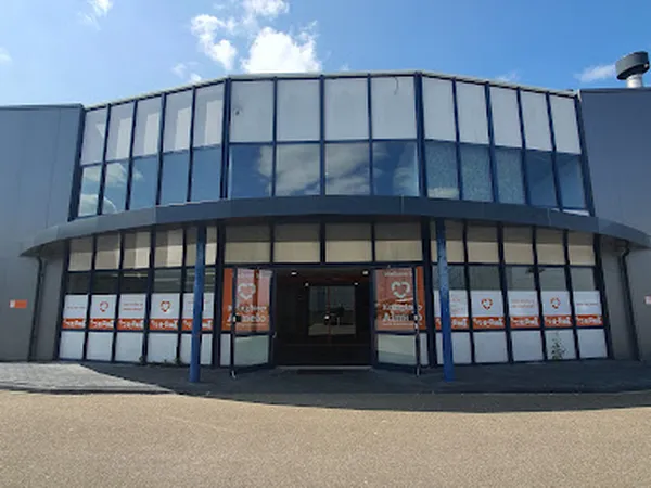 Moderne gevel van kringloopwarenhuis met grote raampartijen en donkerblauwe frame, met informatieposters in de etalage