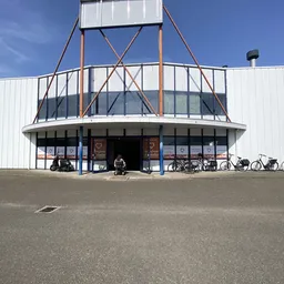 Voorkant van het XL kringloopwarenhuis met karakteristieke ronde vorm, grote ramen en stalen constructie, fietsen geparkeerd 