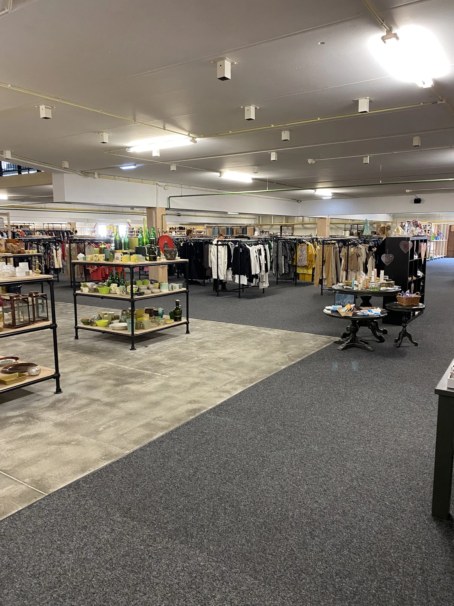 Ruime winkelvloer van kringloopwarenhuis met kledingrekken, uitstallingstafels en diverse artikelen