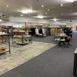 Ruime winkelvloer van kringloopwarenhuis met kledingrekken, uitstallingstafels en diverse artikelen