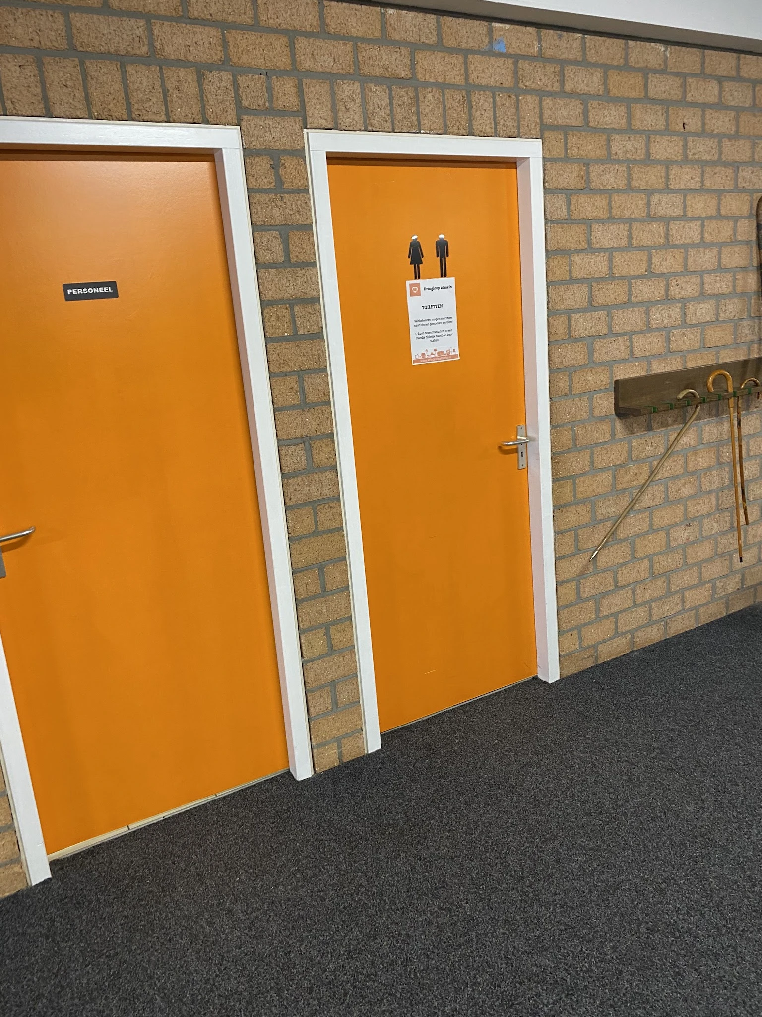 Interieur met oranje deuren, witte kozijnen, bakstenen wand en grijze vloer