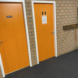 Interieur met oranje deuren, witte kozijnen, bakstenen wand en grijze vloer