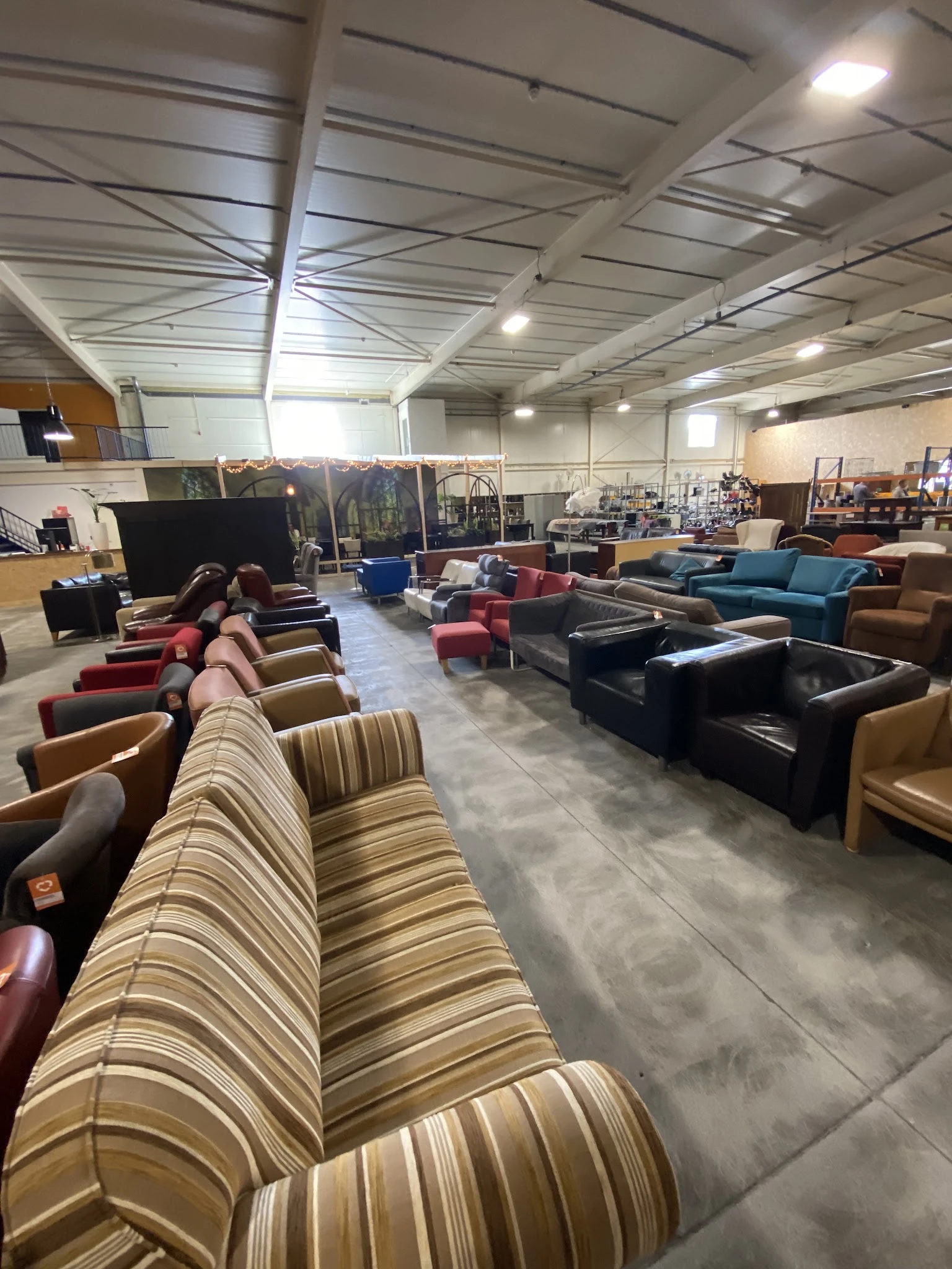 Ruim magazijn met diverse tweedehands meubels: banken, fauteuils en stoelen in verschillende kleuren en stijlen.