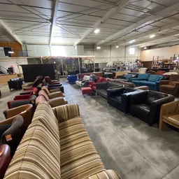 Ruim magazijn met diverse tweedehands meubels: banken, fauteuils en stoelen in verschillende kleuren en stijlen.