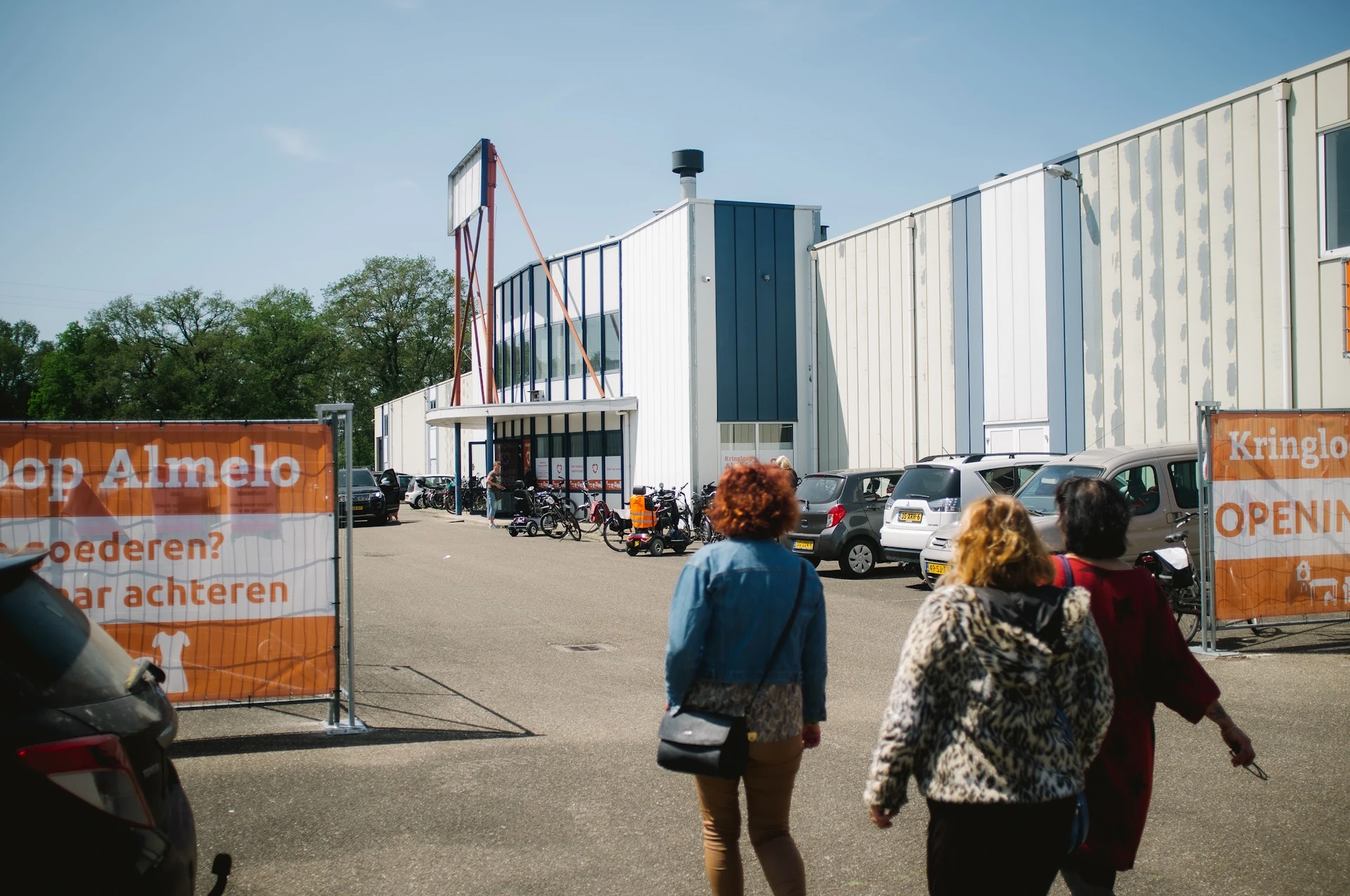 Voorkant van het XL kringloopwarenhuis met witte gevel, parkeerterrein en bezoekers