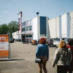 Voorkant van het XL kringloopwarenhuis met witte gevel, parkeerterrein en bezoekers