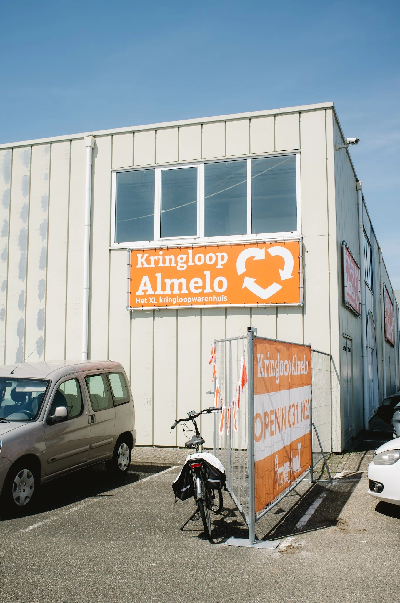 Gevel van kringloopwinkel met oranje bord met hartlogo en tekst 'Kringloop Almelo het XL kringloopwarenhuis'