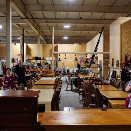 Ruim winkelbinnenruimte met houten tafels, stoelen, en diverse tweedehands spullen op stellingen en aan het plafond