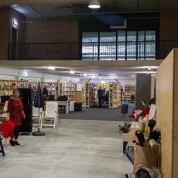 Overzicht van de winkelvloer met boekenrekken, kledingrekken en diverse spullen in een ruim magazijnachtig pand