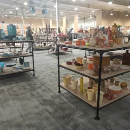 Winkelvloer met meerdere zwart-metalen tafels vol uitgestalde huishoudspullen en decoratieve items in een groot magazijnachti