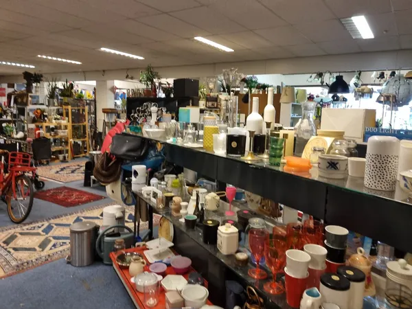 Overzicht van kringloopwinkel met zwarte toonbank vol vazen, kandelaars en decoratieve spullen, op de achtergrond stellingen 