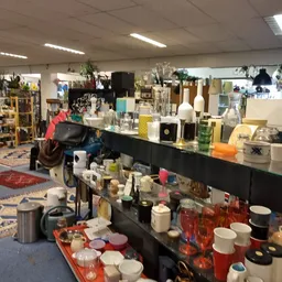 Overzicht van kringloopwinkel met zwarte toonbank vol vazen, kandelaars en decoratieve spullen, op de achtergrond stellingen 