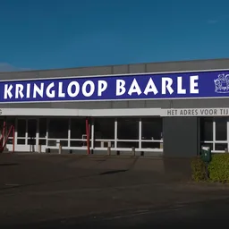 Gevel van kringloopwinkel met blauwe letters en grote ramen, op heldere dag