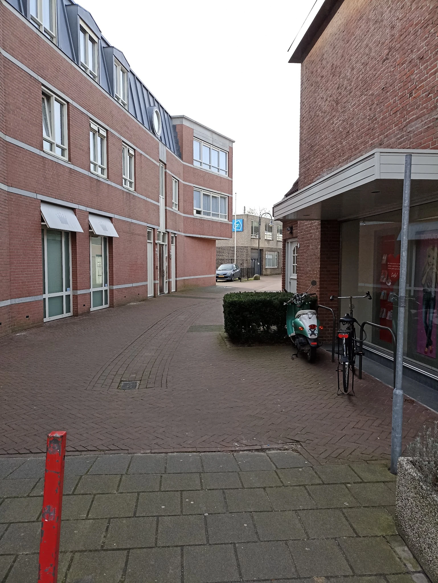 Voorkant van bakstenen gebouw met ingang, fiets en plantenbak op het trottoir
