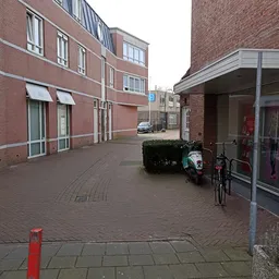 Voorkant van bakstenen gebouw met ingang, fiets en plantenbak op het trottoir