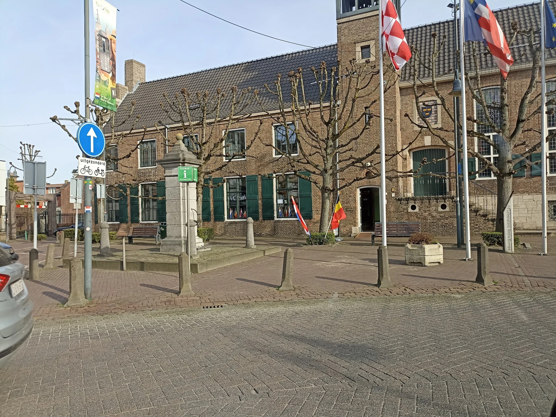 Bakstenen winkelgebouw met groene ramen en deuren aan een plein met vlaggen