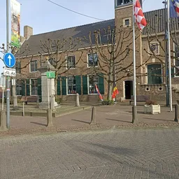 Bakstenen winkelgebouw met groene ramen en deuren aan een plein met vlaggen
