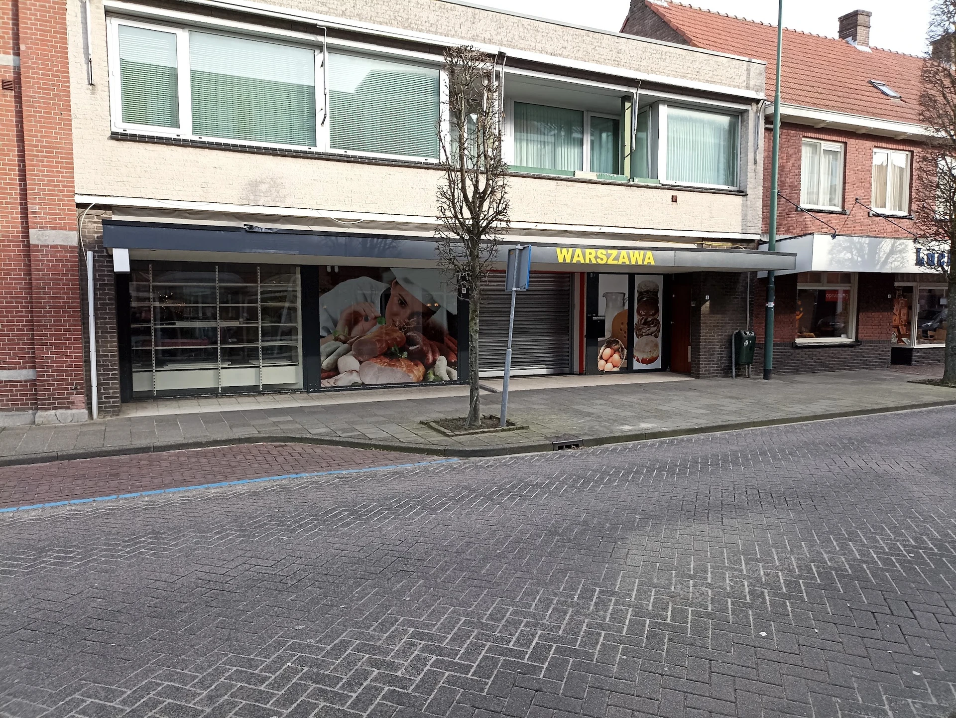 Gevel van kringloopwinkel met donkerblauwe pui, etalageruiten en winkelnaam WARSZAWA op de voorgevel