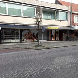 Gevel van kringloopwinkel met donkerblauwe pui, etalageruiten en winkelnaam WARSZAWA op de voorgevel