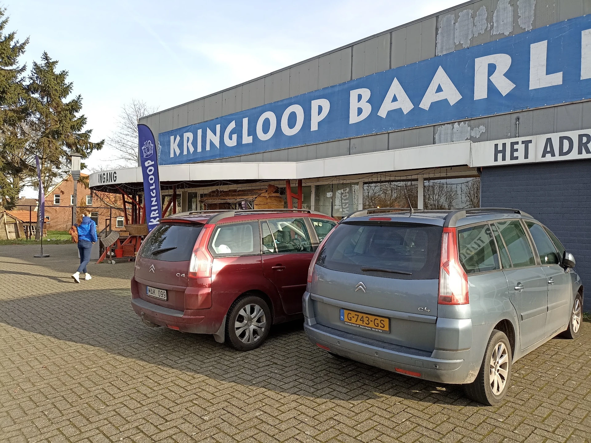Voorgevel van kringloopwinkel met blauwe gevel en parkeerplaats met twee auto's ervoor
