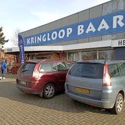 Voorgevel van kringloopwinkel met blauwe gevel en parkeerplaats met twee auto's ervoor