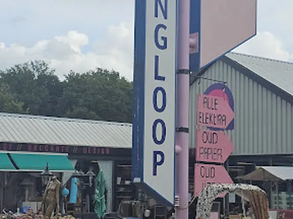 Voorzijde van kringloopwinkel met groot verticaal bord met 'INGLOOP' tekst en roze uithangbord