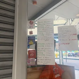 Handgeschreven openingstijden en prijsinformatie op papier tegen een winkelruit