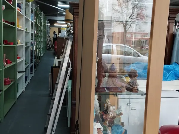 Winkelvloer van kringloopwinkel met groene stellingen, spullen tegen muur en brede etalageruit met uitzicht op straat