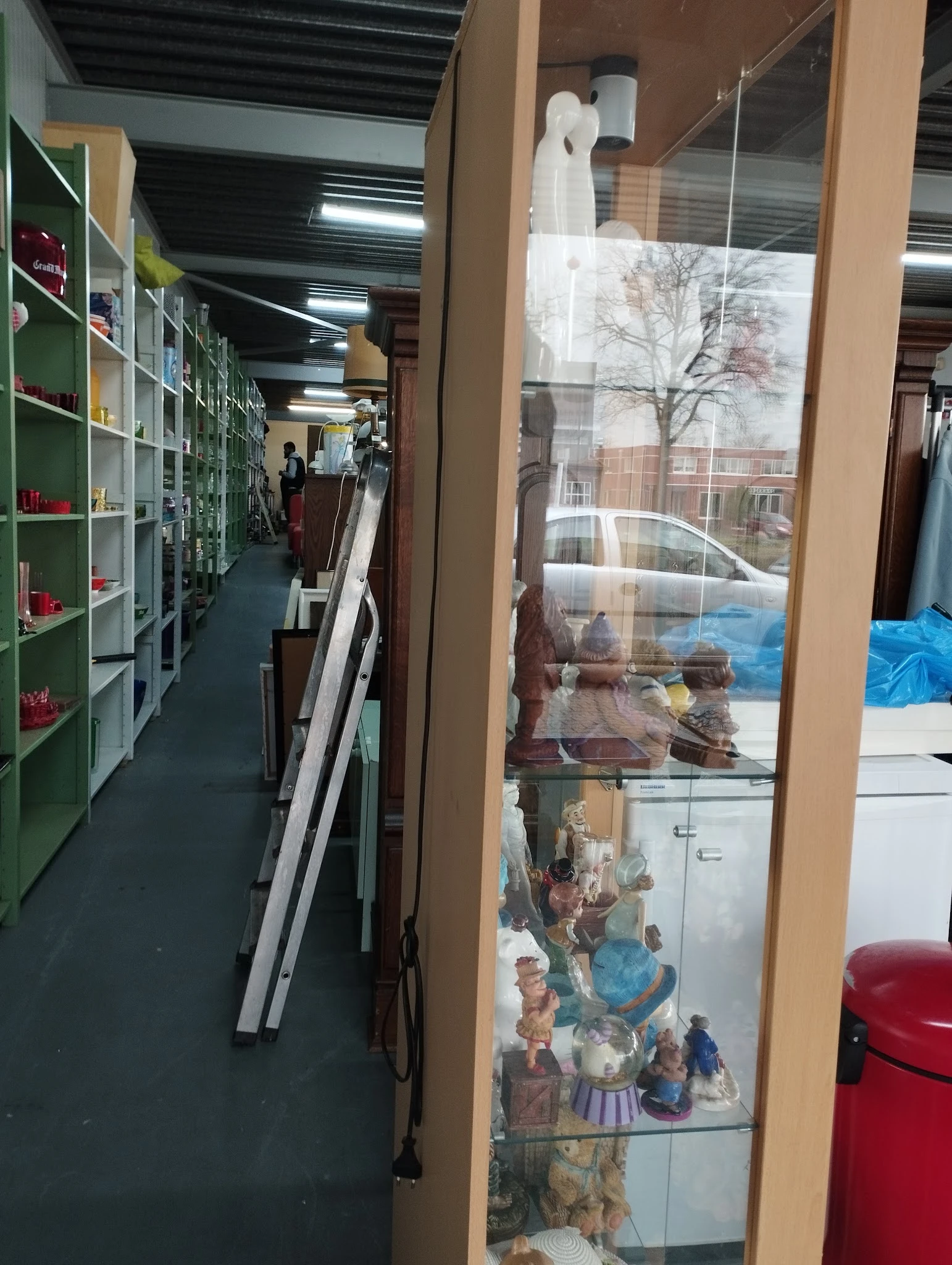 Winkelvloer van kringloopwinkel met groene stellingen, spullen tegen muur en brede etalageruit met uitzicht op straat