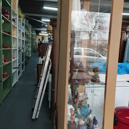 Winkelvloer van kringloopwinkel met groene stellingen, spullen tegen muur en brede etalageruit met uitzicht op straat