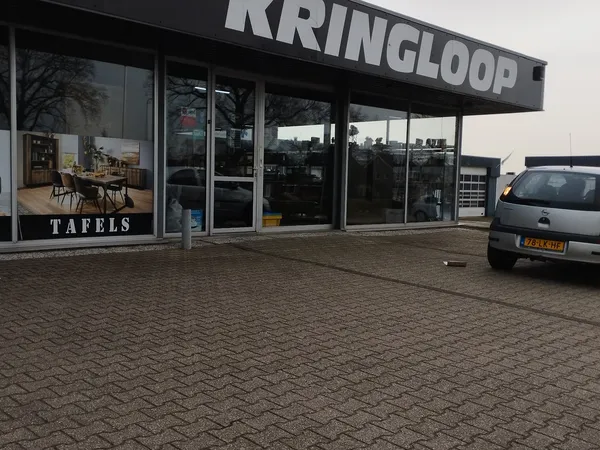 Voorgevel van kringloopwinkel Kringloop met grote ramen, ingang en parkeerplaats ervoor