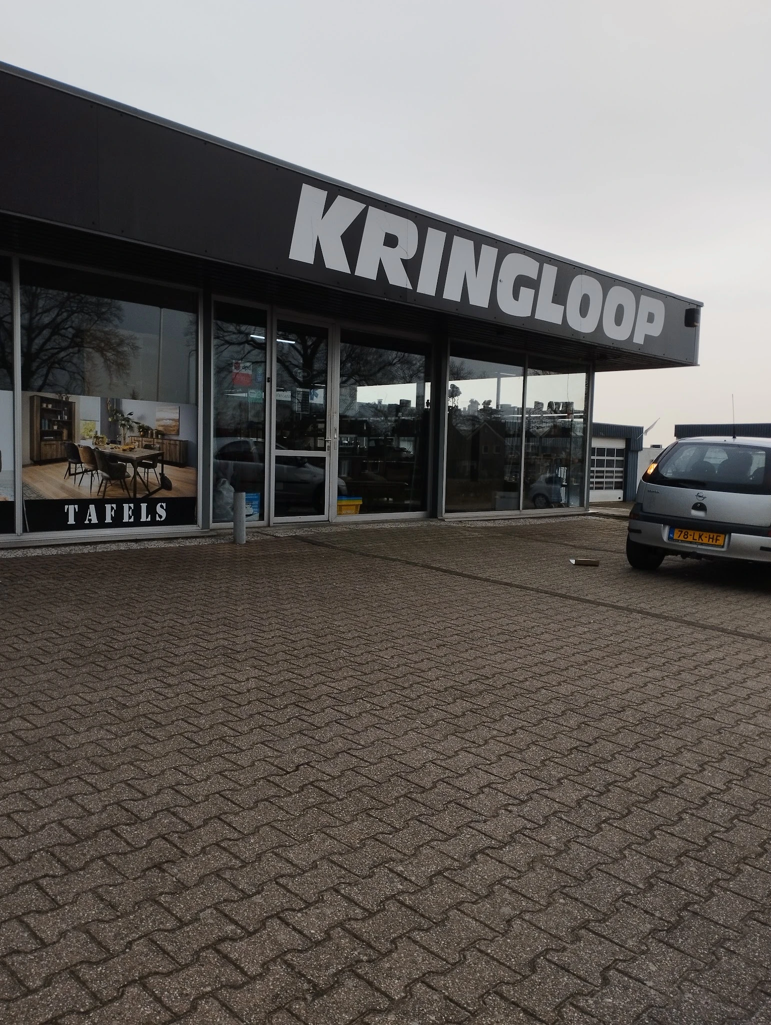 Voorgevel van kringloopwinkel Kringloop met grote ramen, ingang en parkeerplaats ervoor