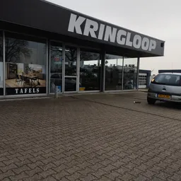 Voorgevel van kringloopwinkel Kringloop met grote ramen, ingang en parkeerplaats ervoor