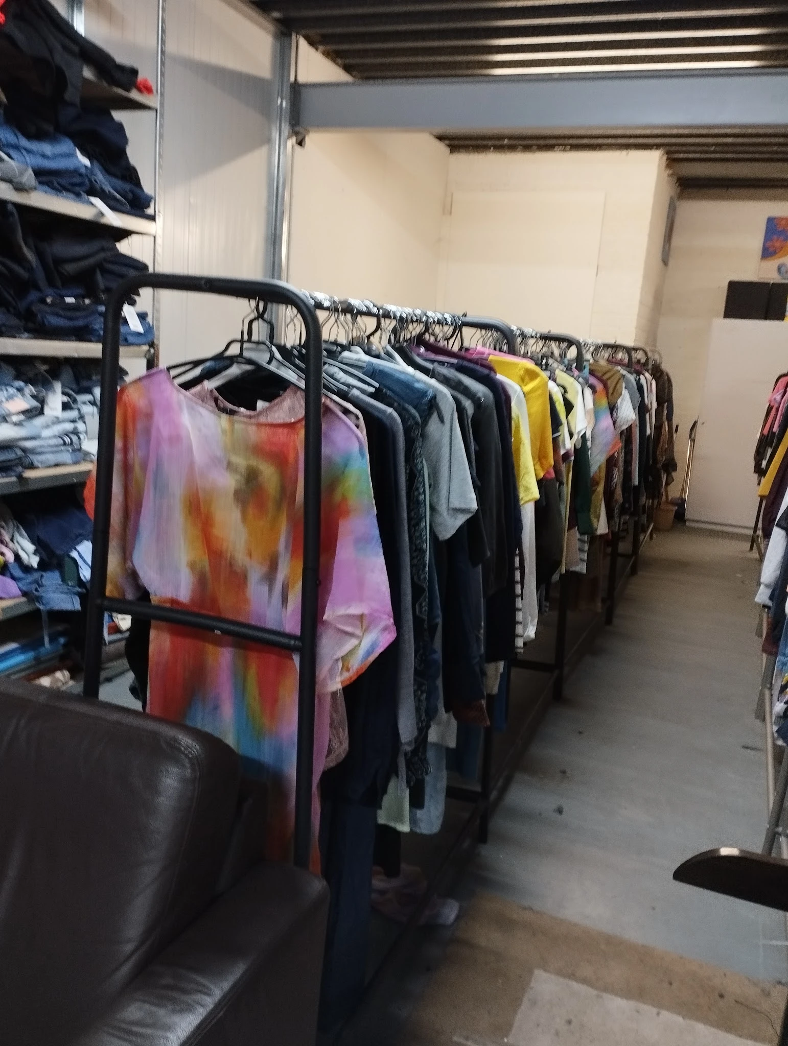 Rekken met tweedehands kleding, waaronder kleurrijke tie-dye shirts en donkere kledingstukken