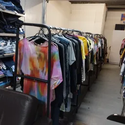 Rekken met tweedehands kleding, waaronder kleurrijke tie-dye shirts en donkere kledingstukken