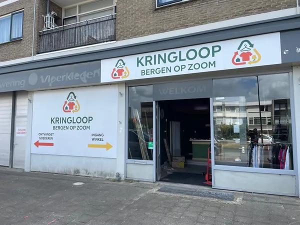 Gevel van kringloopwinkel met witte pui, logo en etalageruiten met kleding zichtbaar