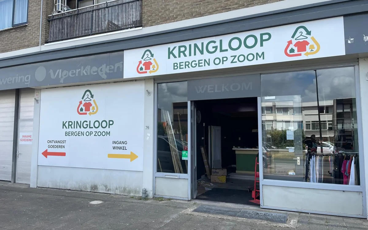 Gevel van kringloopwinkel met witte pui, logo en etalageruiten met kleding zichtbaar